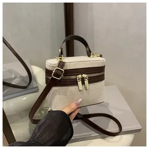 Detail of canvas and brown leather box bag featuring gold dual zippers and top handle