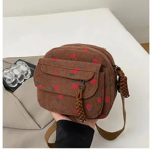 Detail of brown corduroy crossbody bag featuring strawberry embroidery and woven zipper pulls