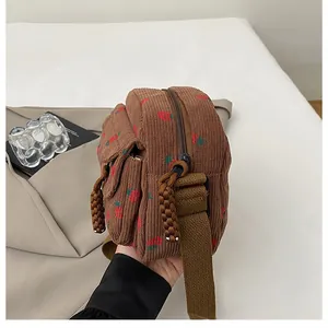 Detail of brown corduroy crossbody bag featuring cute red strawberry prints and rope zipper