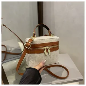 Detail of canvas box bag with brown leather trim, gold zippers, and top handle