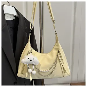 Detail of beige crescent shoulder bag featuring pearl chain and cloud plush pendant accessory