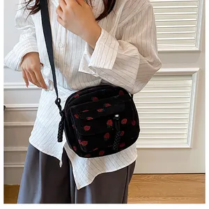 Detail of black corduroy crossbody bag featuring red strawberry patterns and woven zipper pull
