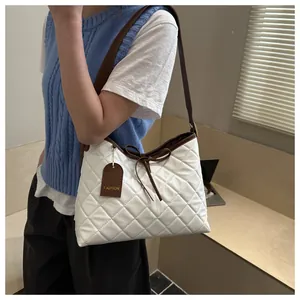 Detail of white quilted tote bag with dark brown strap and decorative leather tag
