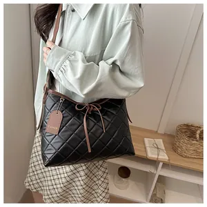 Detail of black quilted crossbody bag with brown straps and bow drawstring closure