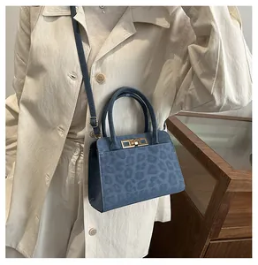 Détail du sac bandoulière gris-bleu à motif animal et fermoir doré sur trench-coat beige
