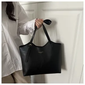 Detail of black leather tote bag with thin straps and gold logo on minimalist background