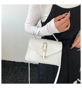 Detail of white leather crossbody bag with golden horseshoe buckle worn by model