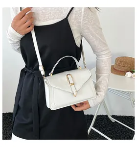 Detail of white PU leather crossbody bag featuring gold hardware and structured V-flap