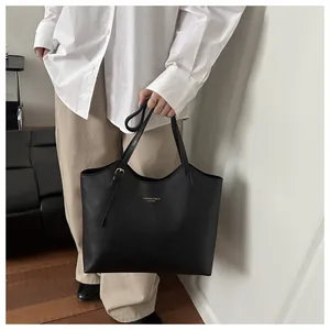 Detail of minimalist black leather tote bag featuring gold embossed text and slim handle