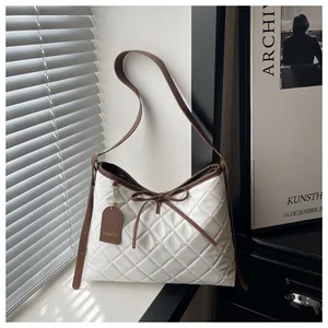 Detail of quilted hobo bag with brown bow accent and leather tag on an indoor window sill