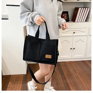 Détail du cabas en toile noire avec deux poches avant et écusson logo en cuir marron