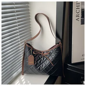 Detail of black quilted tote bag with brown leather trim and fashion brand tag