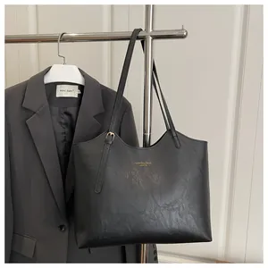 Detail of minimalist black tote bag featuring golden brand print on smooth leather texture