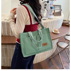 Detail of light green canvas tote bag with multi-pocket design and leather logo tag