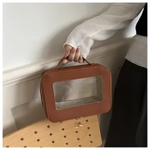 Brown rectangular handbag with clear window and dual metal zippers shown by a model