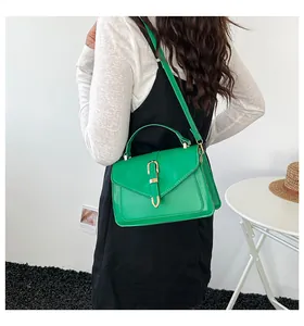 Detail of green minimalist crossbody bag with gold U-shaped buckle in a lifestyle setting