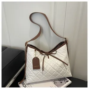 Close-up of cream quilted tote bag with brown trim, leather bow, and fashion tag detail