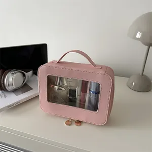 Pink Saffiano portable makeup bag with clear window and golden zippers on a white desk