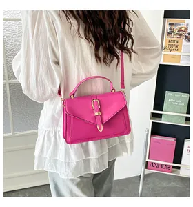 Detail view of pink leather crossbody bag with gold buckle on a white shirt background