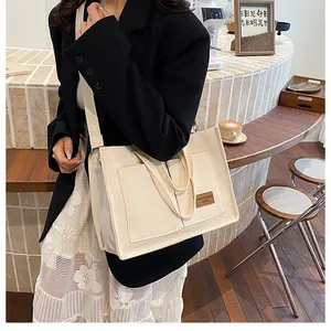 Close-up of beige canvas tote bag with leather logo patch and adjustable shoulder strap