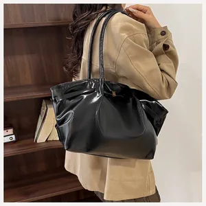 Borsa a spalla nera lucida con texture a pieghe indossata su un trench beige elegante