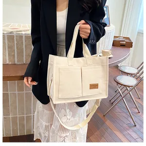 Détail du sac fourre-tout en toile crème montrant les poches et la bandoulière réglable
