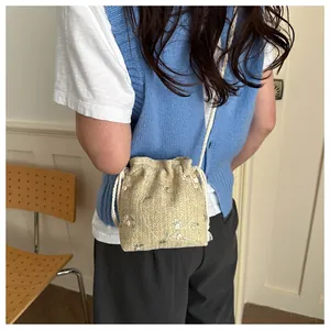 Detail of straw woven bucket bag featuring floral embroidery and drawstring closure