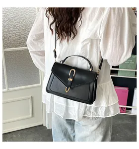 Detail of a black square crossbody bag featuring a triangle flap and gold U-shaped buckle