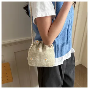 Detail of beige daisy embroidered bucket bag with drawstring closure and rope strap