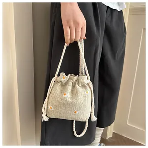 Detail of drawstring bucket bag featuring white daisy embroidery and woven fabric texture