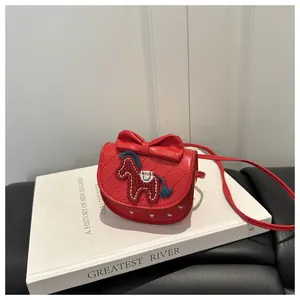 Détail du sac rouge matelassé avec nœud et broderie de poney posé sur un livre décor
