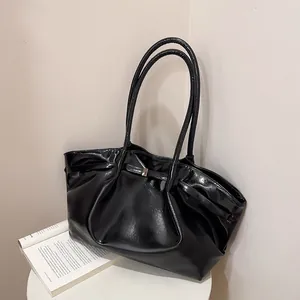 Borsa tote in pelle verniciata nera lucida con fibbia dorata e tracolla su tavolo