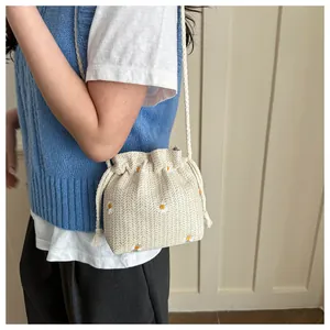 Detail of cream knitted bucket bag with daisy embroidery worn by a model in soft light