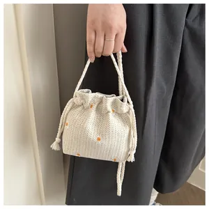 Close-up of cream woven bucket bag with daisy embroidery and drawstring tassel detail