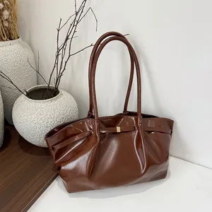 Borsa tote in pelle marrone lucida con accenti dorati su una scrivania minimalista