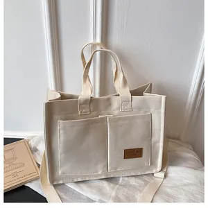 Détail du cabas en toile beige avec poches avant et étiquette de marque en cuir marron