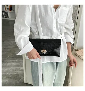 Detail einer schwarzen Falten-Clutch aus Kunstleder mit Goldverschluss am weißen Hemd