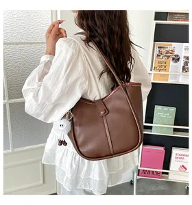 Detail of a dark brown matte leather shoulder bag with a cute white pom-pom charm detail