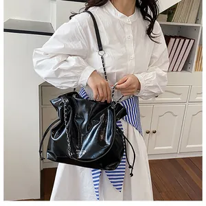Détail d'un sac cabas en cuir verni noir avec chaîne argentée et cordons sur le côté