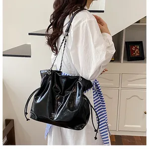 Gros plan sur un sac cabas noir brillant avec logo argenté et bandoulière en chaîne