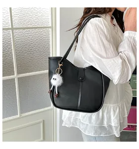 Minimalist black tote bag with white plush charm shown in a modern interior setting
