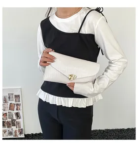 Detail der cremefarbenen Clutch mit Wellenprägung und goldenem Herz-Verschluss aus Leder