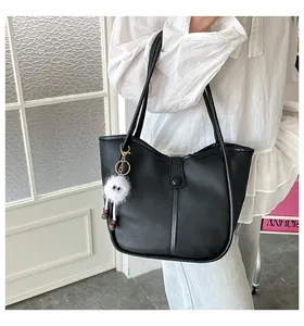 Detail of black matte PU leather tote bag with a white fluffy monster charm accessory