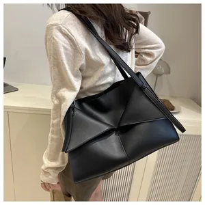 Detailed view of black geometric folding leather tote bag worn as a shoulder underarm bag