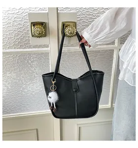 Detail of black faux leather tote bag with white plush monster charm on gold handle