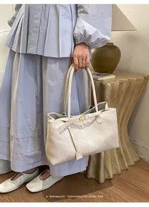 Close-up of minimalist beige tote bag with leather straps and gold buckle detail