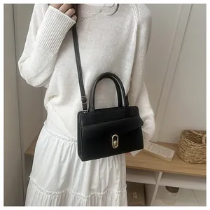 Detail of black pebble grain handbag with golden twist lock on white outfit