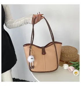 Close-up of beige tote bag with brown contrast trim and cute white plush monster charm
