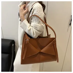 Close-up of caramel faux leather shoulder bag featuring a decorative metal eyelet strap