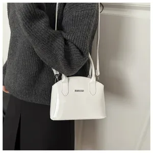 Close-up of a white patent leather shell bag featuring the metallic FASHION logo on a strap